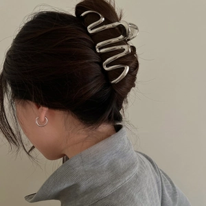 Detail shot of a large silver wavy metal claw clip holding a hair bun on a female model