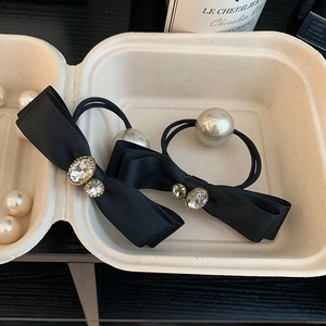 Detailed close-up of a satin bow hair tie featuring rhinestones and a large pearl