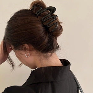Macro view of a large black wave-shaped hair claw clip styling brown hair for women