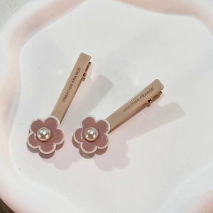 Pink floral hair clips with white pearls and Creation France lettering on a white tray
