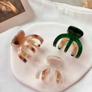 Three acetate mini hair claws in tortoiseshell, green, and white on a ceramic tray