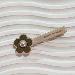 Detail of floral hair clip with pearl center and 'CREATION FRANCE' print