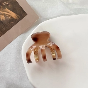 Close-up of small amber tortoiseshell claw clip on a white ceramic plate with gold metal spring