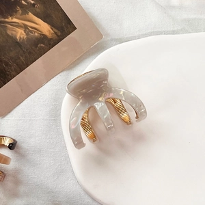 Detailed macro view of acetate shark claw clip with marble texture and gold metal teeth