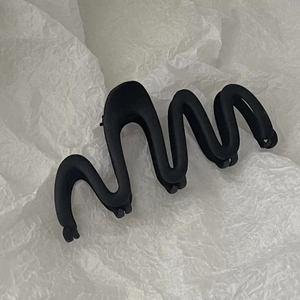 Macro shot of large wave-shaped matte black hair claw clip with frosted texture detail