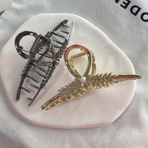 Elegant wheat stalk metal hair claws with rhinestones and pearls on a ceramic tray