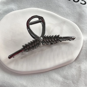 Detail view of a metallic wheat ear hair claw clip with a pearl on a white ceramic plate