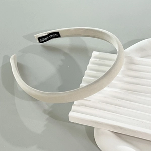 Detail showing the white fabric headband with a black hand-made woven label on textured surface