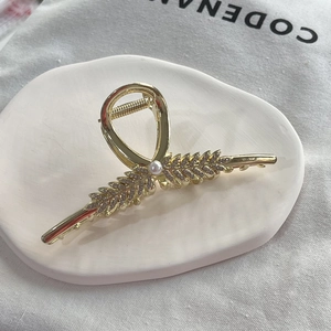 Detail of golden wheat ear hair claw with rhinestones and central pearl on display