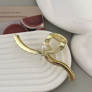 Eleganter Haarklammer aus Goldmetall mit großer Perle auf dekorativem weißem Teller