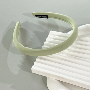 Close-up of a light green fabric headband featuring a black handmade textile label