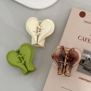 Detailed view of heart-shaped acrylic hair claws in cream, green, and amber tones