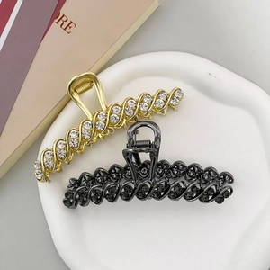 Elegant gold and gunmetal wave-shaped hair claws with rhinestones on ceramic tray