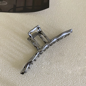 Detailed side view of a glossy gun grey metallic claw clip with irregular wave edges