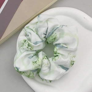 Dettaglio di scrunchie bianco con motivi floreali verde chiaro e blu in tessuto