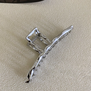 Detailed close-up of large silver liquid metal hair claw clip with wave texture