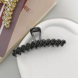 Detail of grey rhinestone hair claw clip on ceramic plate showing intricate spiral design