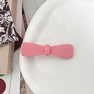Detailweergave van glanzende roze strik haarspeld op een wit keramisch bord met rekwisieten