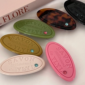 Detailed view of colorful oval hair clips with embossed letters and a small rhinestone