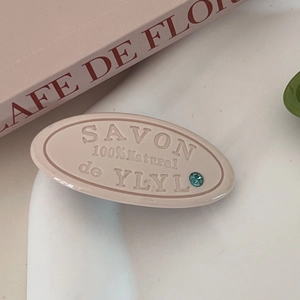Detail of oval hair clip with embossed letter carvings and blue rhinestone accent