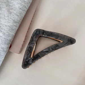 Detail view of large triangle acetate hair claw clip with black marble texture and gold spring