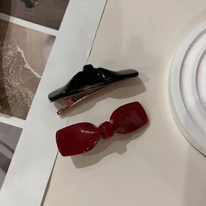 Elegantes Set aus schwarzen und tiefroten Acetat-Haarspangen für Damen auf beigem Grund