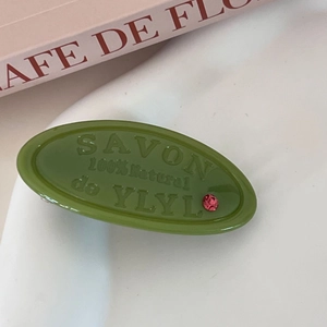 Close-up of matte green oval hair clip with embossed SAVON lettering and pink crystal