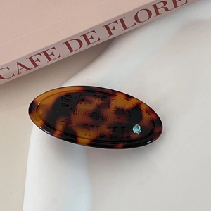 Detailed view of tortoiseshell resin oval clip with SAVON text and blue rhinestone