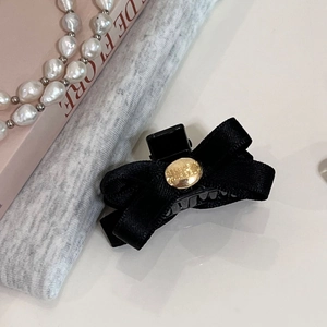 Détail d'une pince à cheveux à nœud en satin noir avec un bouton doré gravé