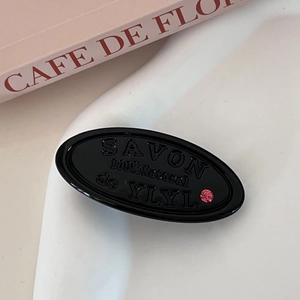 Detail of black oval hair clip with embossed letters and a small pink rhinestone detail