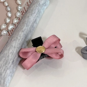 Détail de la pince à cheveux noeud rose avec plaque dorée sur une table crème