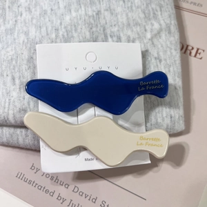 Detail of wavy acetate hair clips in navy blue and cream on branding card