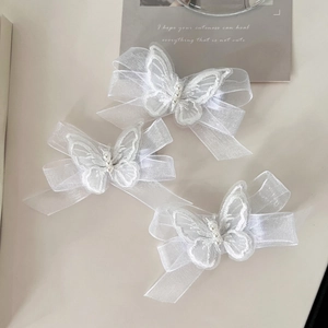 Detail of three white mesh bow hair clips with embroidery and pearls on a minimal backdrop