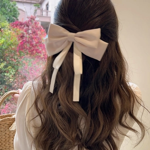 Elegant cream silk bow hair clip with long ribbons worn on wavy brunette hair