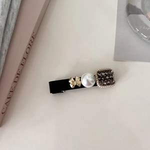 Detail of elegant black duckbill hair clip with golden bow, pearls, and crystals