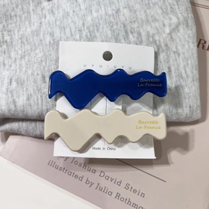 Close-up of wavy acetate hair clips in navy and beige with gold lettering details