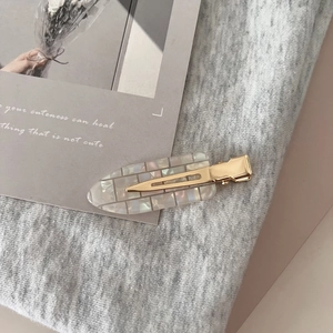 Minimalist white acetate hair clip with shell texture on a golden metal base