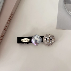 Close-up of pearl hair clip with purple crystal and gold-tone brand plate detail