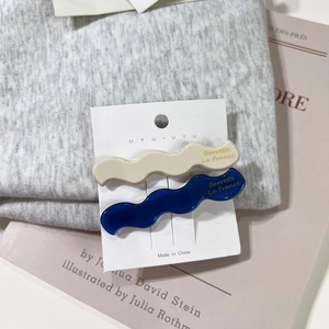 Detail view of wavy acetate hair clips in beige and blue on a branded display card