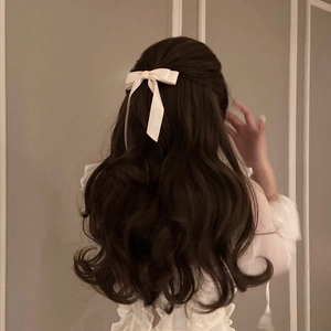 Detail view of a cream satin bow hair clip with long ribbons on wavy brown hair