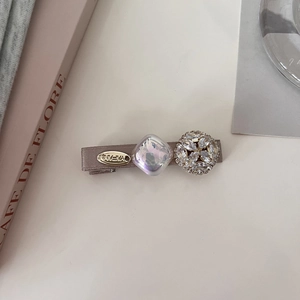 Detail of elegant gray satin duckbill hair clip with crystal studs and golden oval emblem