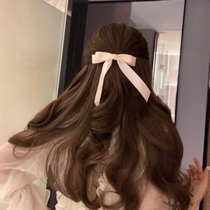 Close-up of a dusty pink satin bow hair clip with long ribbons on long wavy hair