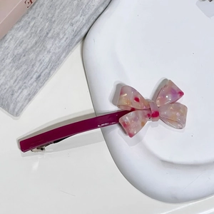 Détail d'une barrette à ressort en acétate faite main avec un nœud floral sur plat blanc