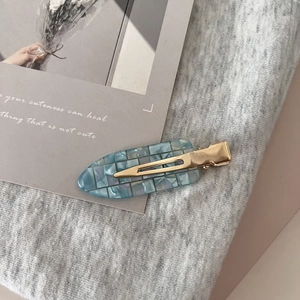 Macro detail of blue checkered cellulose acetate hair clip with gold metal base