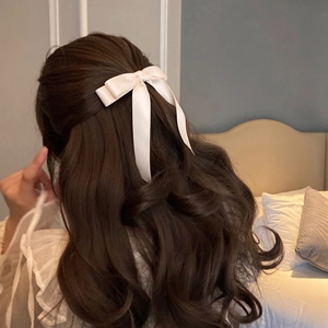 Detail view of a cream satin bow hair clip with long ribbons worn on model's hair