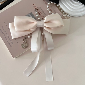 Detail of cream satin bow hair clip with elegant pearl chain and vintage gold coin pendant