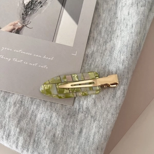 Close-up of green marble acetate hair clip with golden metal crocodile grip on grey fabric