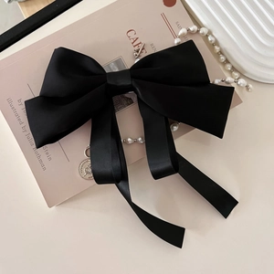 Macro detail of elegant black satin bow hair clip with flowing ribbons on light background
