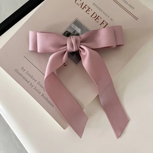 Detail of a pink satin bow hair clip with long ribbons on a minimalist magazine