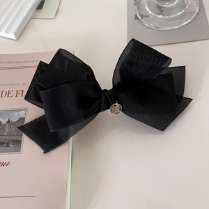 Détail d'une pince à cheveux avec nœud en tulle noir multicouche et pendentif argenté chic
